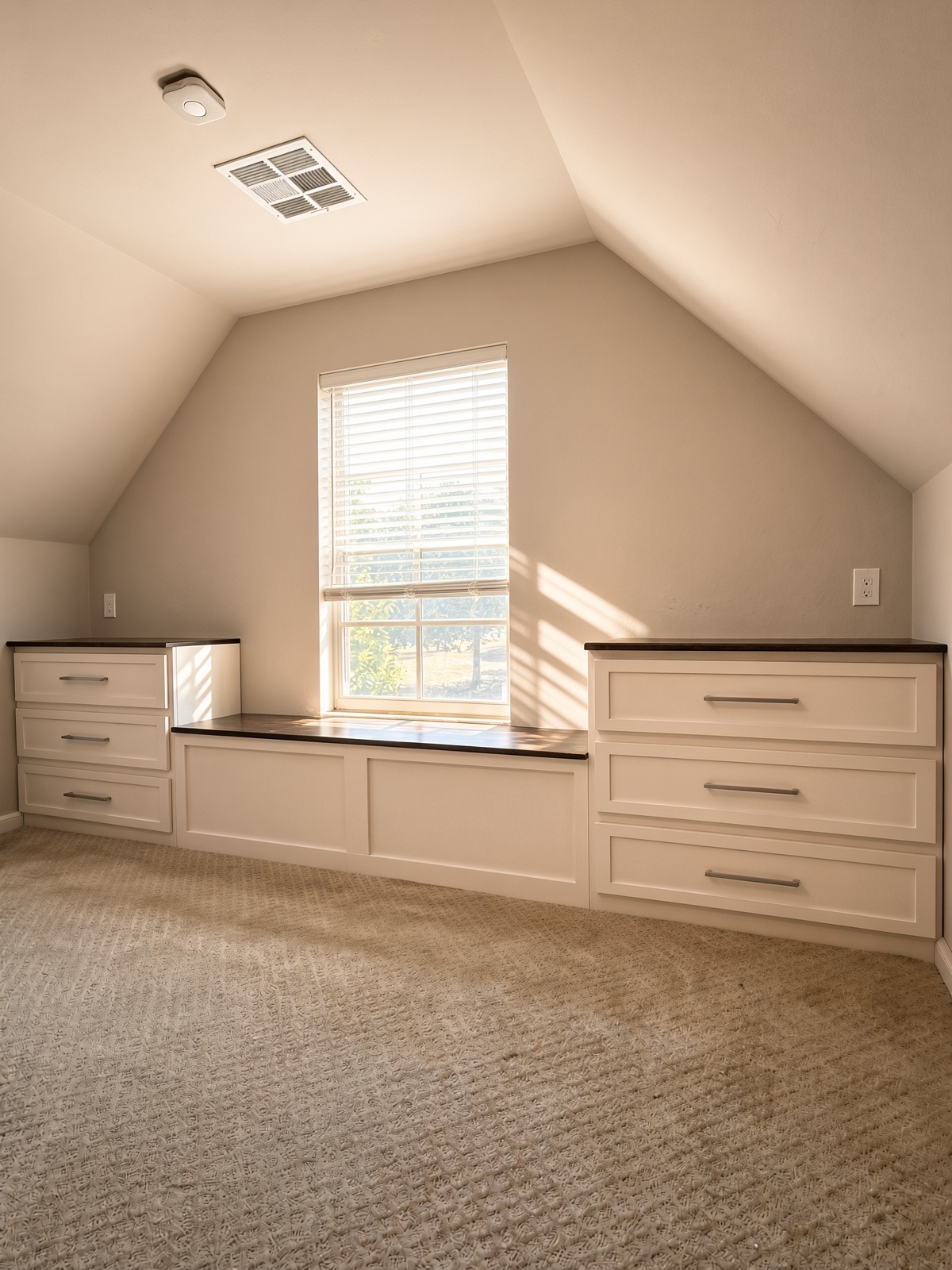 White built-in dresser units and window seat under a sloped ceiling